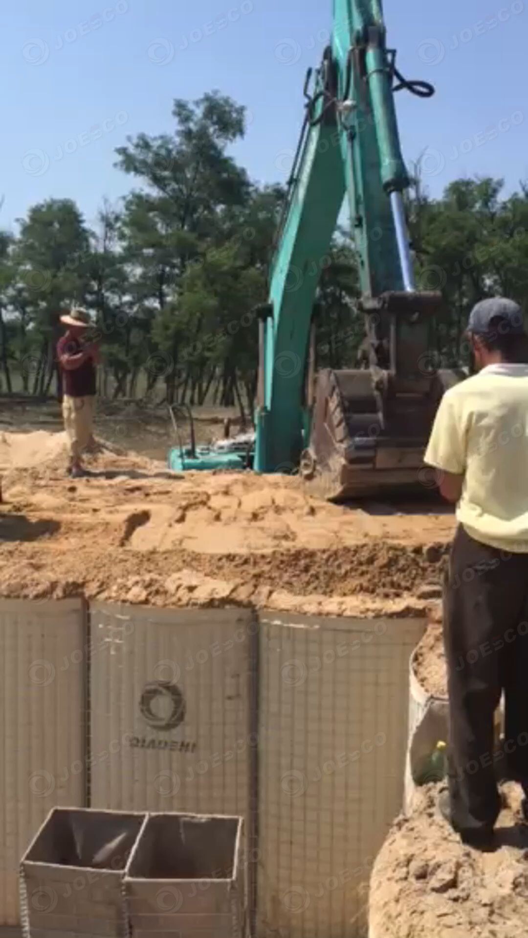 Workers are using a shovel bucket to smooth and compact the sand on the upper layer of the military barrier thumbnail 1
